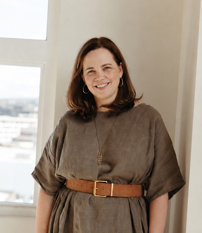 Sarah Kaehn standing by a window in a linen dress